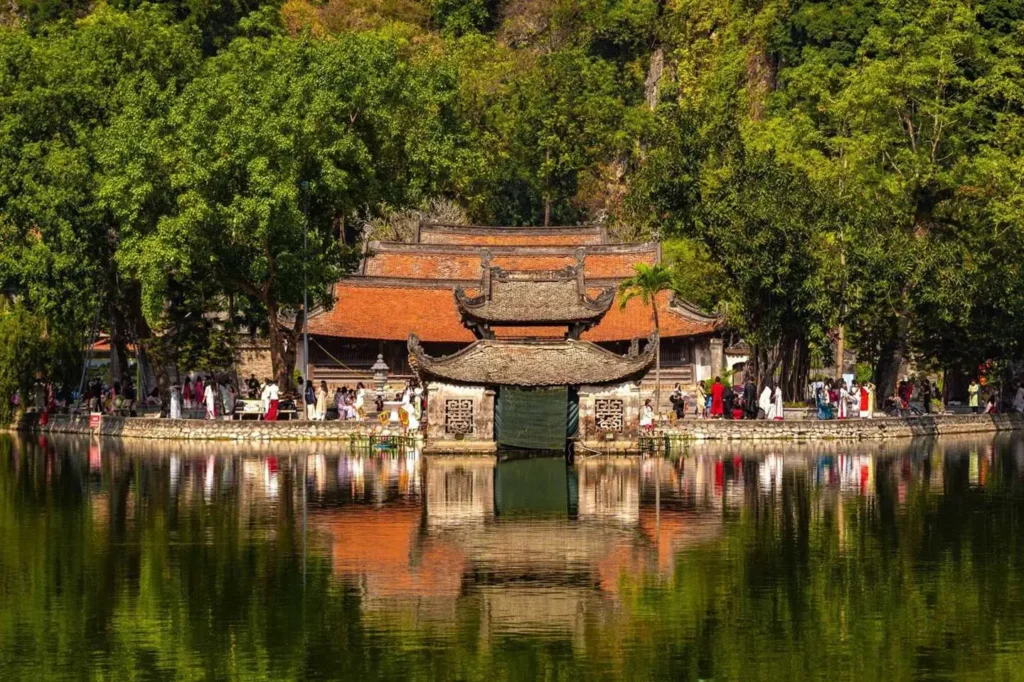 Thủy đình chùa Thầy mái ngói cổ soi bóng xuống hồ, phía sau là mái chùa đỏ và rừng cây