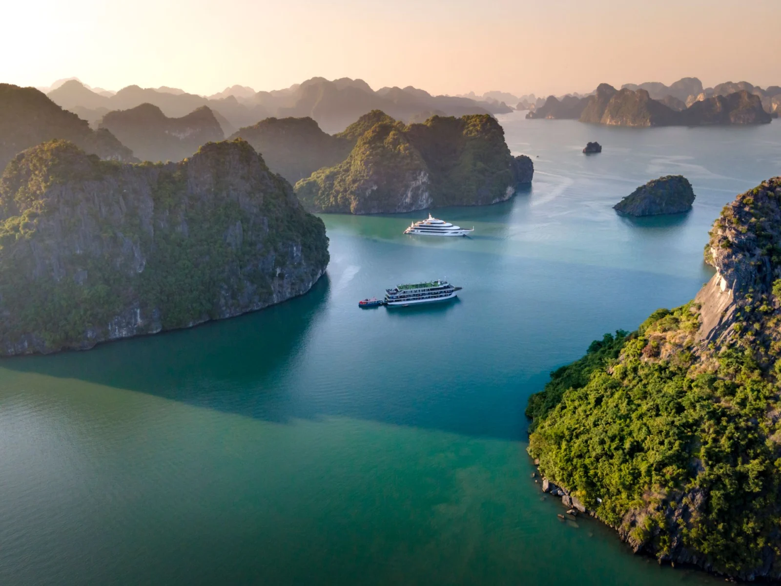 Hai du thuyền giữa vịnh Hạ Long, xung quanh là đảo đá vôi phủ cây xanh và mặt nước xanh ngọc